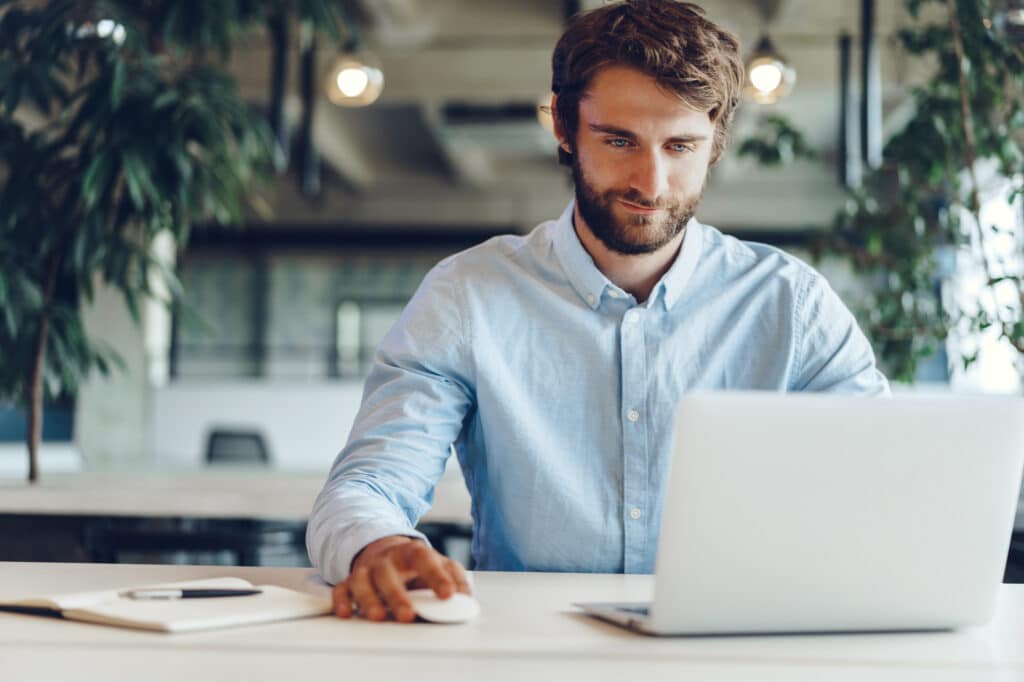 A man sitting at a table looking at this laptop