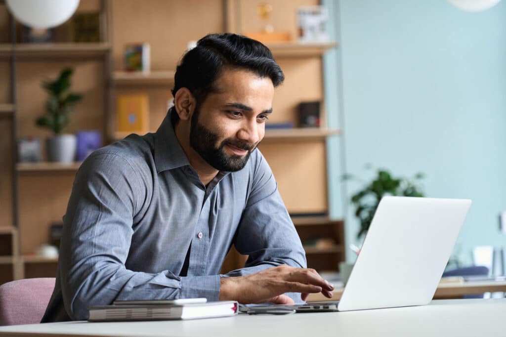 Smiling indian business man working studying on laptop computer