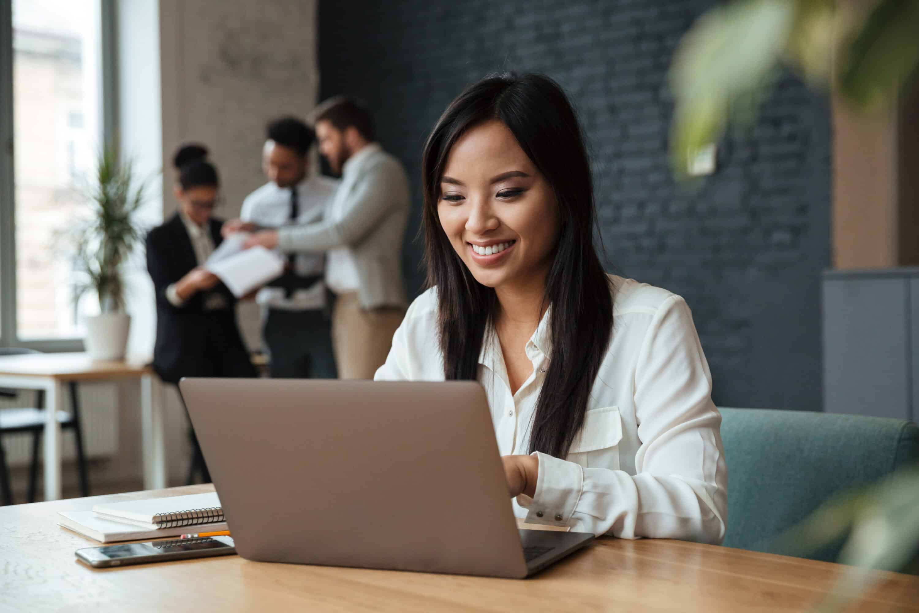 Cheerful young asian business woman using laptop